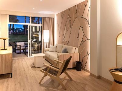 Světý obývací pokoj se světlým dřevěným nábytkem, pohovkou a přístupem na balkon za soumraku.