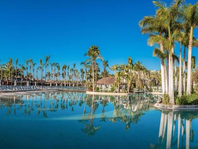 Großer Hotelpool mit Palmen umgeben und klar blauem Himmel im Hintergrund