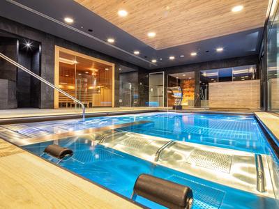 Moderní vnitřní bazén s vířivkou, dřevěným stropem a velkou skleněnou stěnou.