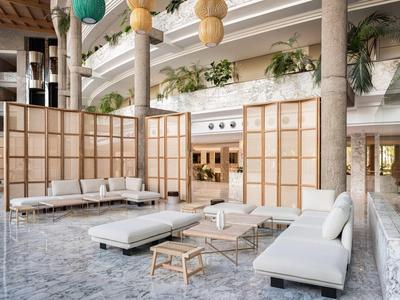 Světlá posezení s bílými pohovkami, nízkými stoly a dřevěnými příčkami v hotelové hale.