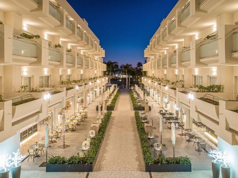 Symetrický pohled na osvětlený hotelový dvůr s posezením v noci.