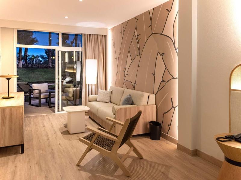 Světý obývací pokoj se světlým dřevěným nábytkem, pohovkou a přístupem na balkon za soumraku.