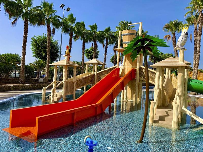 Vodní park s barevnými skluzavkami a palmami v hotelovém bazénu.