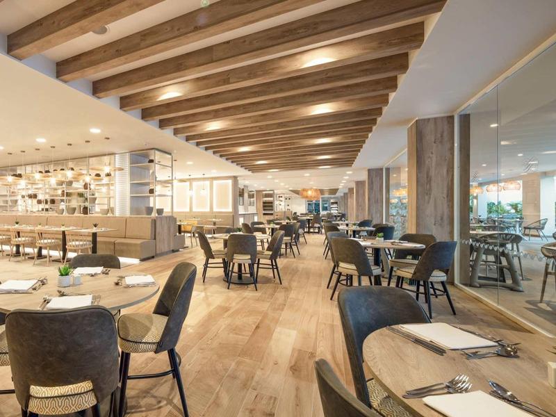 Moderní hotelová restaurace s dřevěným stropem, pohodlnými židlemi a prostřenými stoly.