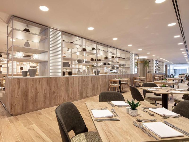 Moderní, světlá jídelna s dřevěnou podlahou a bílým nábytkem v hotelu.