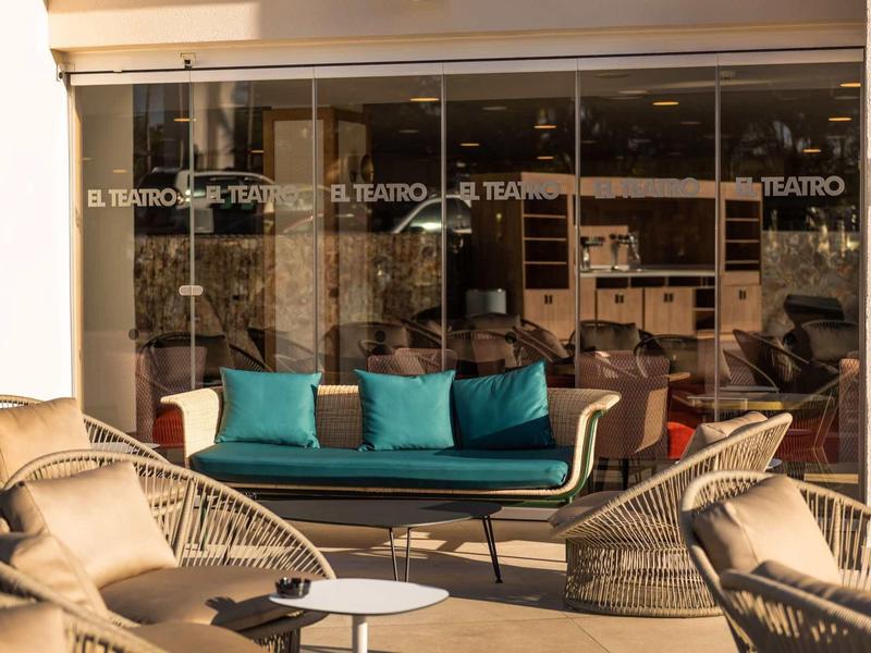 Pohodlný venkovní prostor s moderními židlemi a pohovkou před skleněnou fasádou.