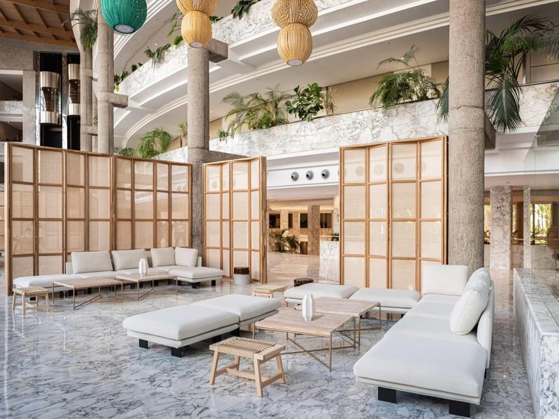 Světlá posezení s bílými pohovkami, nízkými stoly a dřevěnými příčkami v hotelové hale.