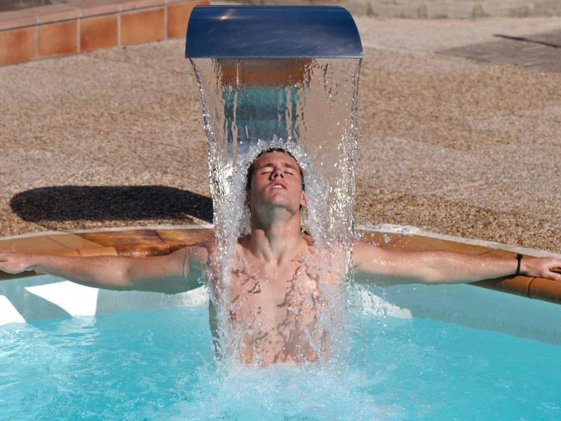 Homme profite d'une cascade dans la piscine de l'hôtel par une journée ensoleillée.