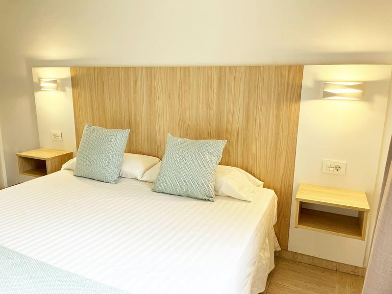 Chambre d'hôtel moderne avec grand lit, deux coussins verts, tête de lit en bois et lampes murales