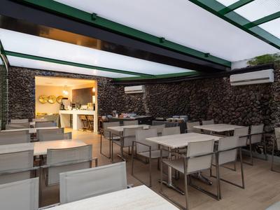 Moderní zastřešená venkovní terasa s bílými stoly a židlemi v restauraci.