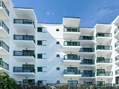 Vícepodlažní bílá hotelová budova s balkony a skleněnými zábradlími pod modrou oblohou.