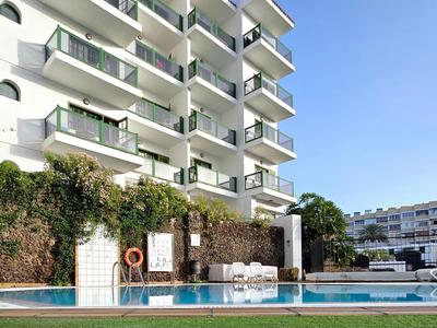Edificio de hotel de varios pisos con piscina y césped bajo cielo despejado.