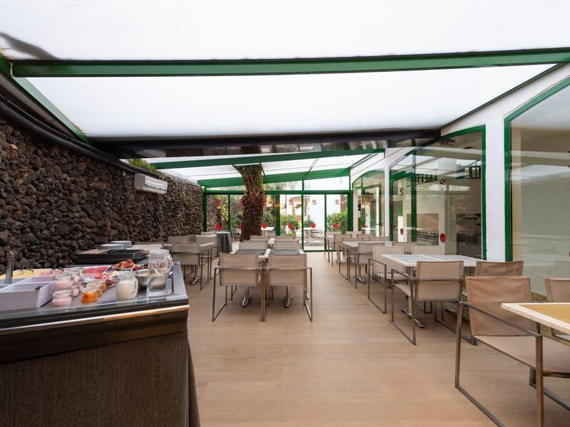 Moderní vnitřní prostor restaurace s stolem, židlemi a stojanem na noviny vedle kamenné zdi.