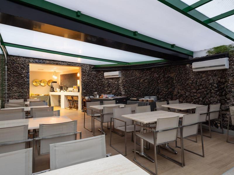 Moderní zastřešená venkovní terasa s bílými stoly a židlemi v restauraci.