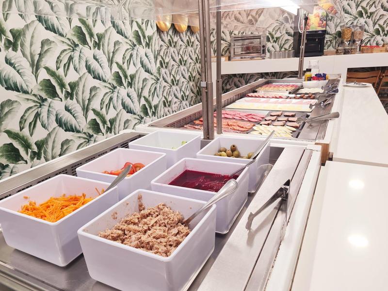 Bufet s různými pokrmy v bílých obdélníkových miskách na dlouhém pultu.