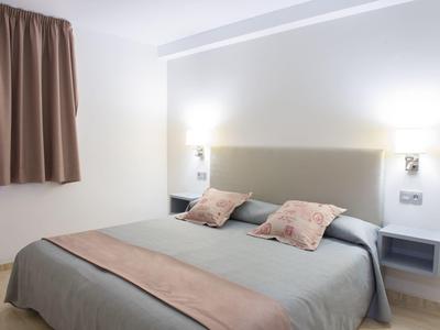 Modern hotelkamer met tweepersoonsbed, hoofdbord, kussens en gordijn aan de muur.