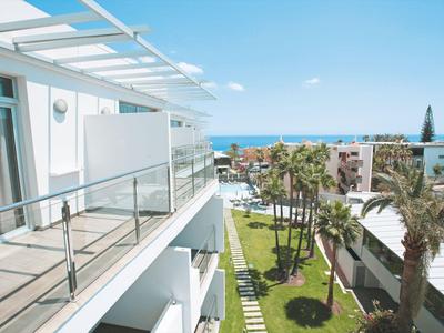 Vue depuis un balcon d'un hôtel moderne sur un jardin avec des palmiers et la mer en arrière-plan.