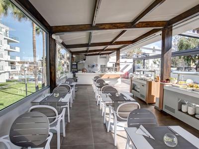 Modern, lichtovergoten serre met zitplaatsen en uitzicht op een hotel tuin.