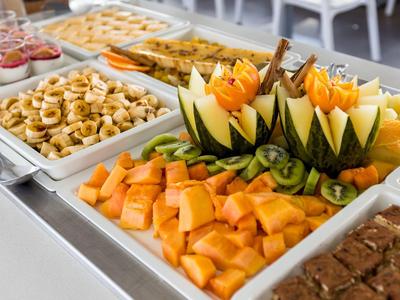 Buffet met gesneden fruit, gebak en desserts op witte schalen.