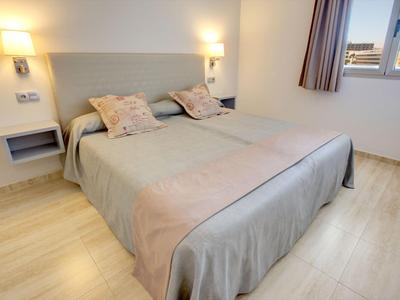 Chambre lumineuse avec grand lit, deux oreillers et fenêtre avec rideaux.