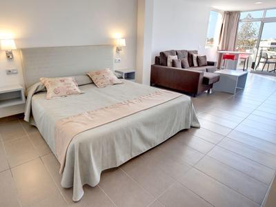 Lichte hotelkamer met tweepersoonsbed, zithoek en balkon met zeezicht.