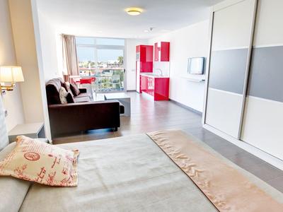 Lichte hotelkamer met bed, bank, rode kitchenette en uitzicht op de stad