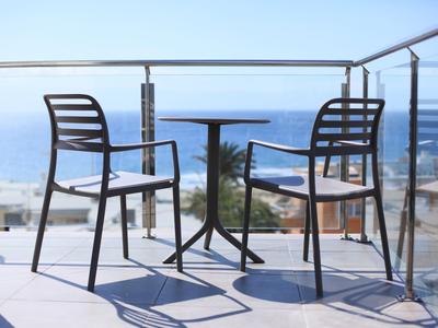 Deux chaises et une table sur un balcon avec vue sur la mer sous un ciel clair.