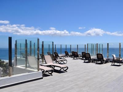 Terrasse ensoleillée avec chaises longues et garde-corps en verre donnant sur la mer.