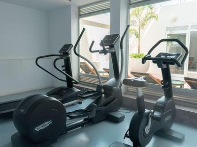 Salle de sport avec appareils d'entraînement comme tapis roulant et vélo stationnaire près de grandes fenêtres donnant sur l'extérieur.