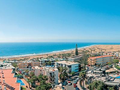 Panoramisch uitzicht op een kustresort met strand, zwembad en hotels bij heldere hemel.