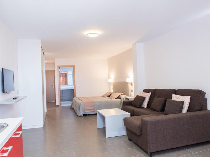 Moderne hotelkamer met zithoek, tweepersoonsbed en aan de muur gemonteerde tv.