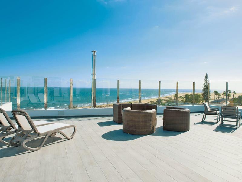 Modern zonneterras van hotel met ligstoelen en uitzicht op zee bij heldere lucht.