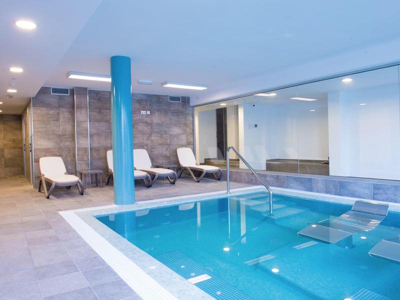 Moderne overdekte zwembad met ligstoelen en blauwe zuilen in een wellnessruimte.