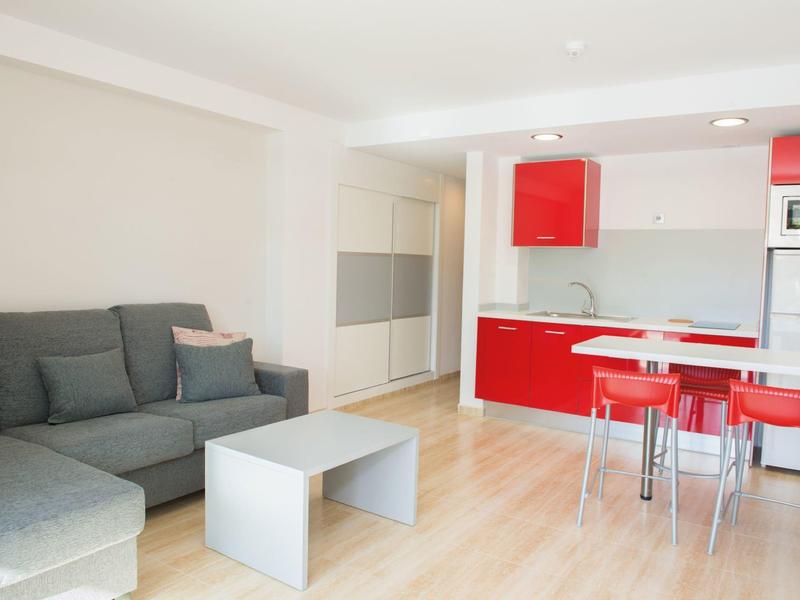 Modern woonkamer met grijze bank, rode keuken en eetgedeelte.