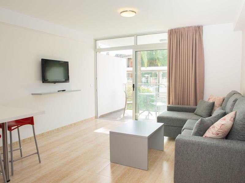 Modern woonkamer met grijze bank, aan de muur gemonteerde tv en toegang tot balkon.