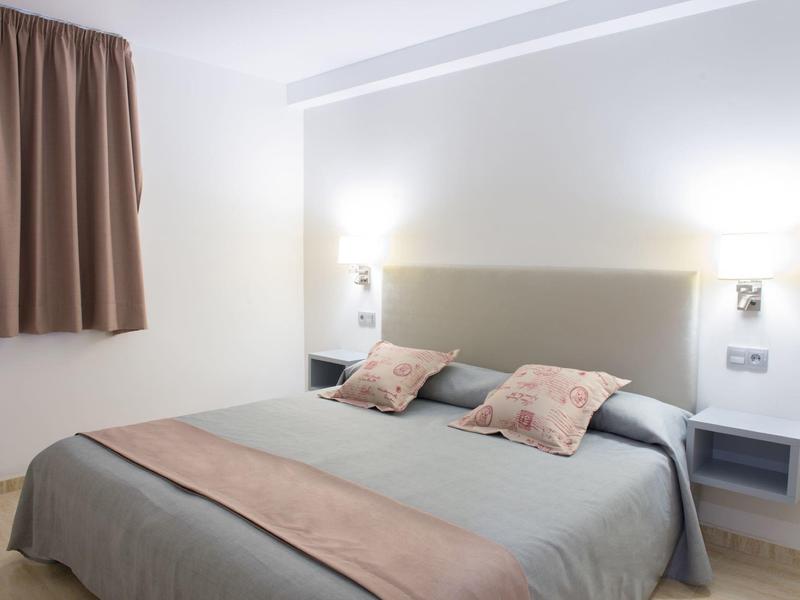 Modern hotelkamer met tweepersoonsbed, hoofdbord, kussens en gordijn aan de muur.