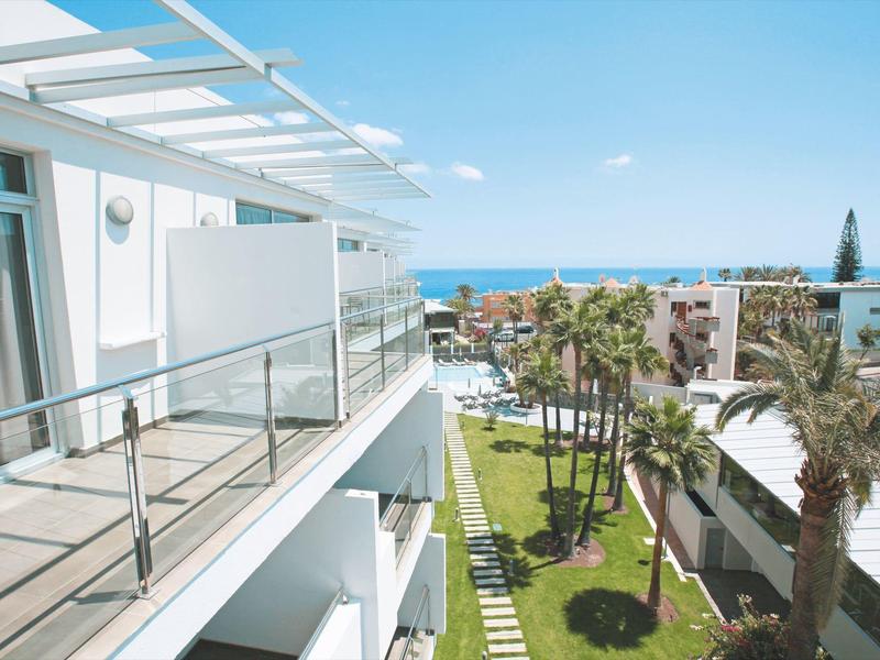 Hotelbalkon met glazen balustrade met uitzicht op verzorgde tuin en zee op de achtergrond.
