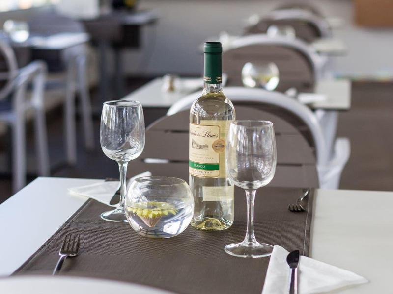 Witte wijnfles en twee wijnglazen op een gedekte tafel in een lichte restaurant.