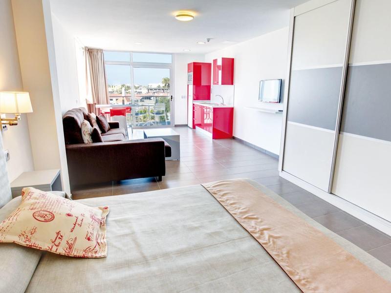 Lichte hotelkamer met bed, bank, rode kitchenette en uitzicht op de stad