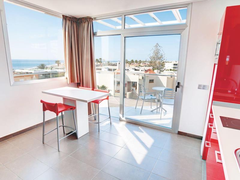 Lichte moderne kamer met groot raam, kleine tafel en uitzicht op terras en zee.