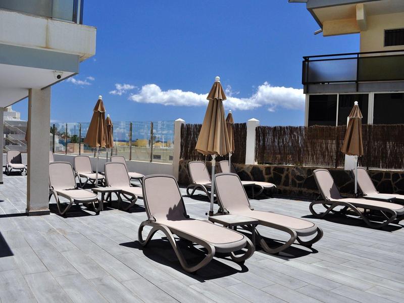 Lege ligstoelen met parasols op een hotelterras onder een zonnige lucht.