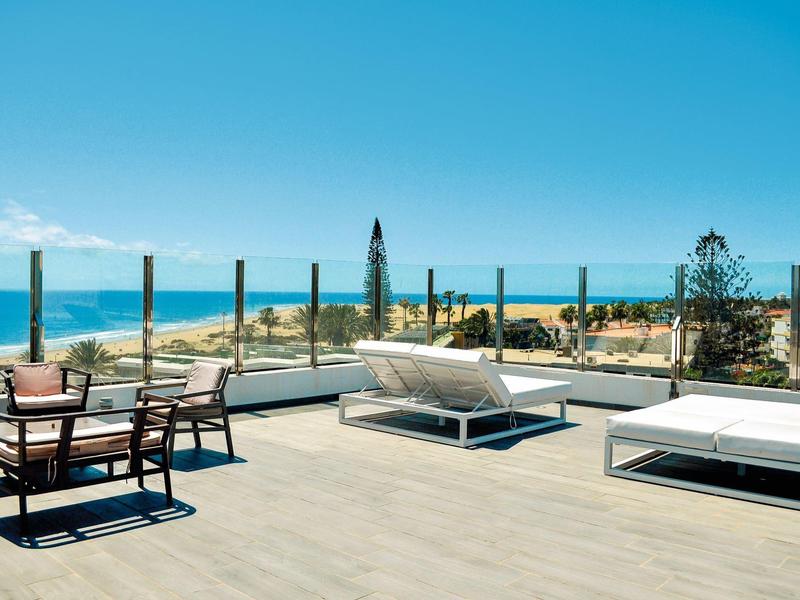 Groot terras met comfortabele stoelen en uitzicht op zee onder een heldere hemel.