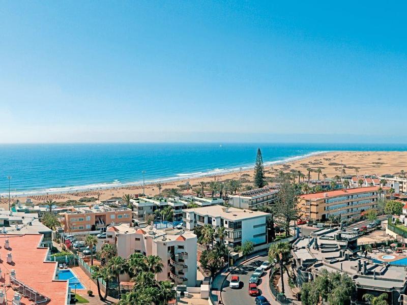 Panoramisch uitzicht op een kustresort met strand, zwembad en hotels bij heldere hemel.