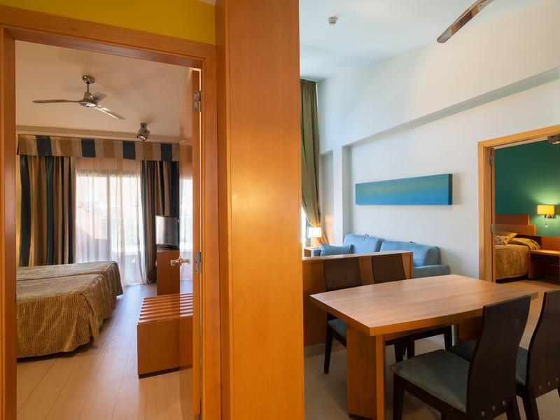 Hotel room with two connected areas: a bedroom and a dining space with table and chairs.