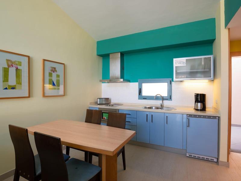 Compact kitchen and dining area with wooden table, two chairs, and blue cabinets.