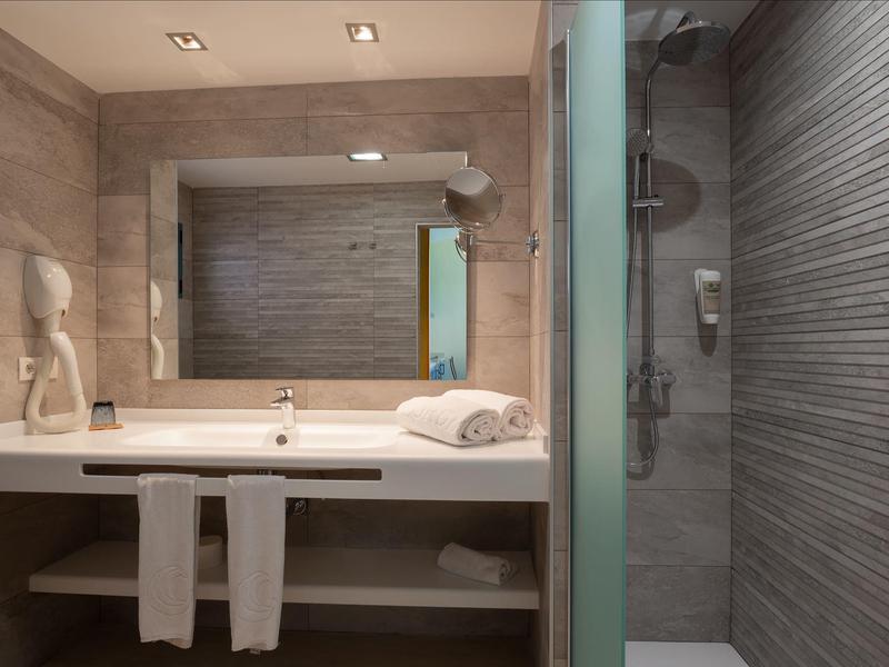 Modern hotel bathroom with sink, large mirror, towels, and shower area with glass door.