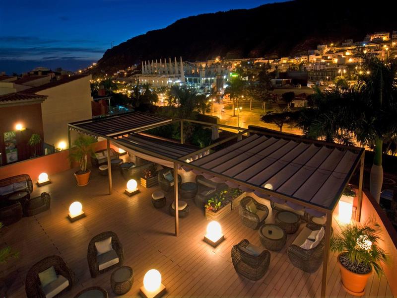Cozy rooftop terrace with seating and warm lights overlooking a lit hillside at night.