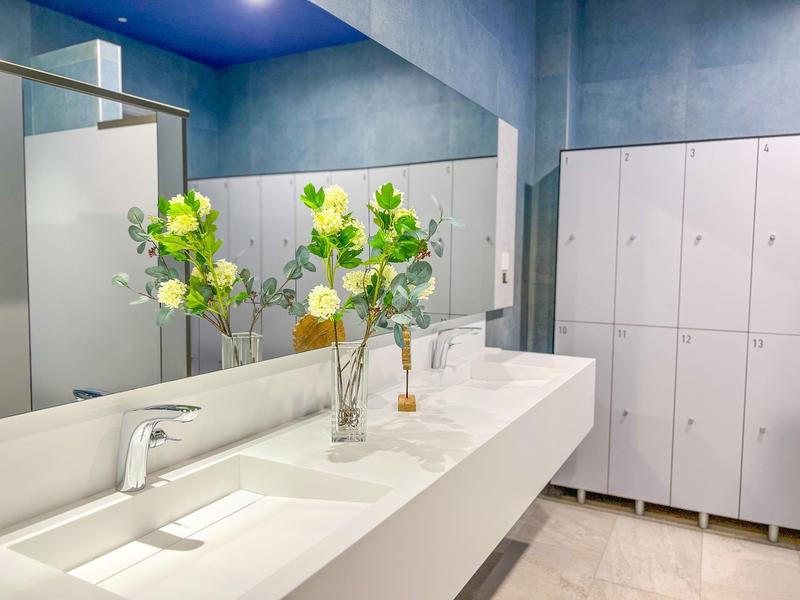 Modern white sink area with faucets, mirror, and lockers in a clean changing room.