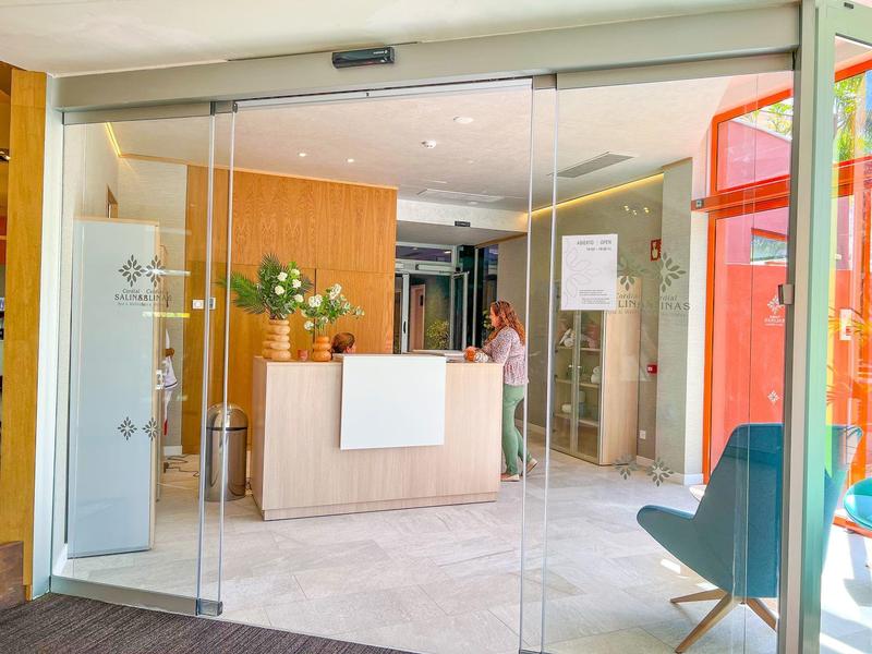 Modern hotel reception with glass doors, wooden desk, and a chair in a bright lobby.