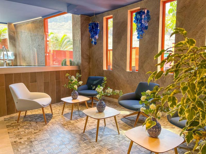 Cozy hotel lounge with armchairs, coffee tables, potted plants, and decorative blue wall accents.